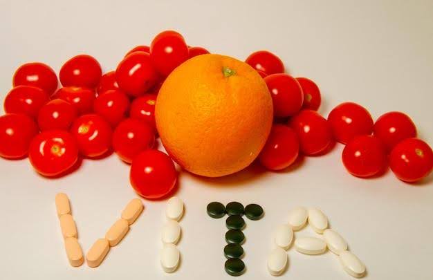 An orange and cherry tomatoes arranged with dietary supplements spelling 'VITA,' symbolizing the connection between natural sources and vitamins supplements