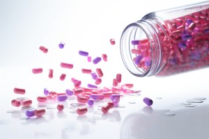 A transparent bottle tipped over with colorful soft gel capsules and vitamins spilling onto a white surface, representing health supplements and pharmaceutical products to tell websites to buy supplements