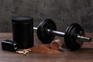 White Label Supplements in USA – protein powder, capsules, and black supplement containers alongside a dumbbell on a wooden surface, representing fitness and bodybuilding nutrition.