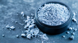 Close-up of finely textured blue powder in a black container with scattered granules – premium product concept from custom powder manufacturers.