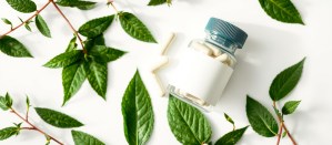 Glass bottle of white capsules surrounded by green herbal leaves – clean and natural product concept representing Ethical Supplement Manufacturers' commitment to plant-based and transparent sourcing.