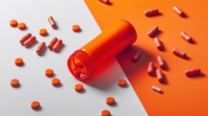 Spilled orange capsules and tablets from a translucent bottle on a vibrant dual-tone background – high-quality product concept by leading Vitamin A manufacturers.