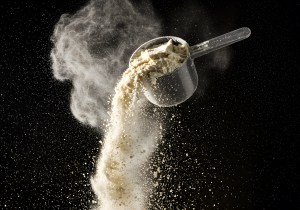 Scoop of protein powder dispersing in the air against a black background – dynamic visual representing premium quality Private Label Protein Products.