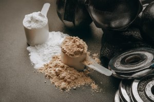 Scoops of protein and supplement powder beside gym weights and dumbbells – symbolizing fitness-focused American supplement manufacturers, supplement manufacturers in the USA, and supplement contract manufacturing with quality and consistent lead times.