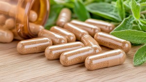 Close-up of vegetable capsules spilling from an amber bottle onto a wooden surface, with fresh green leaves in the background, representing plant-based supplement manufacturing