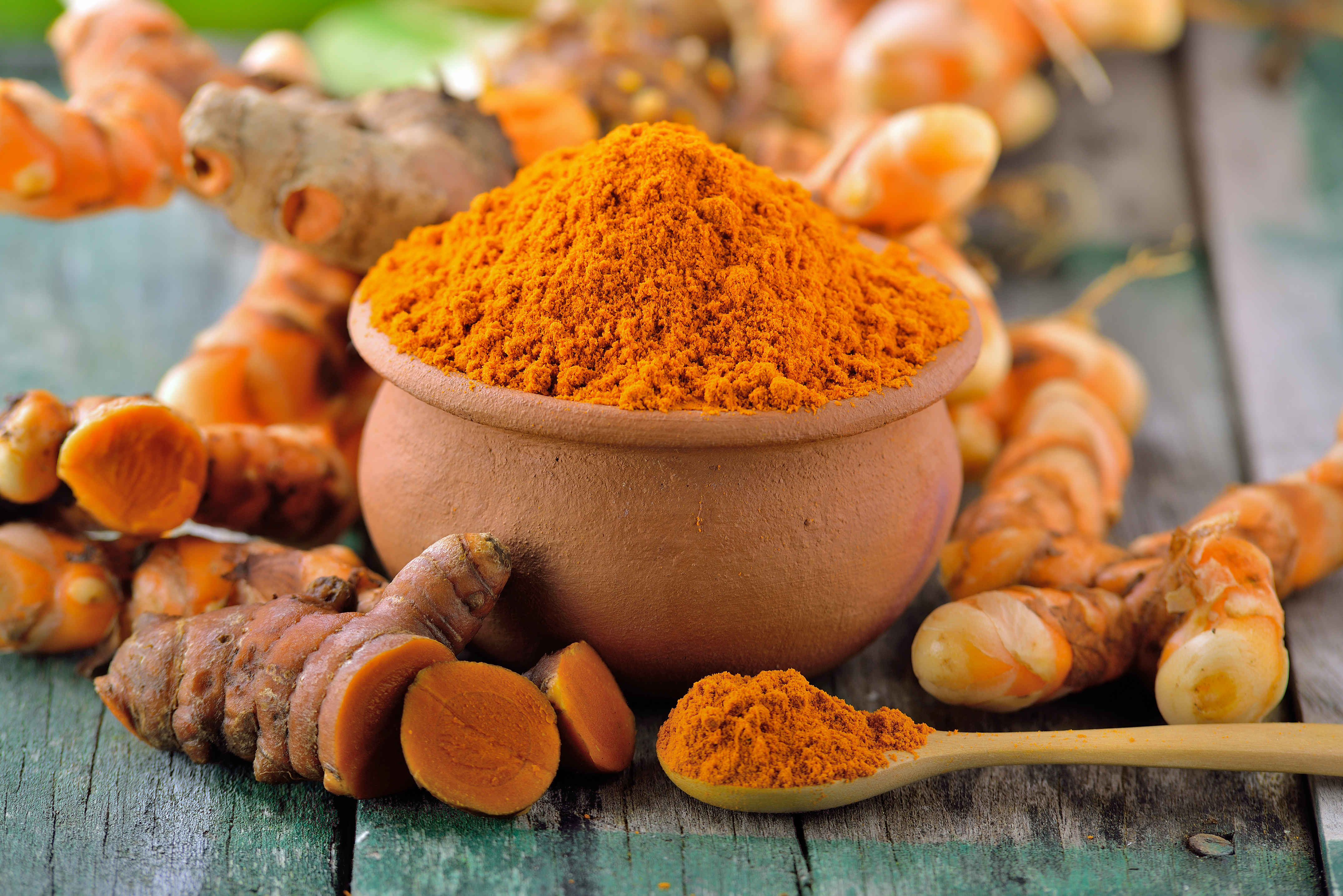 Private label turmeric powder in a clay pot with fresh turmeric roots on a rustic wooden surface, showcasing high-quality organic turmeric for health and wellness products.