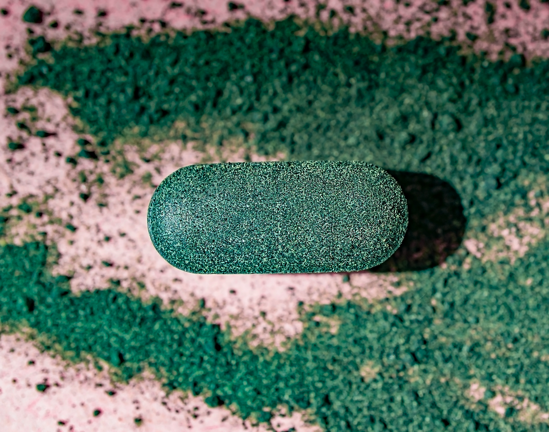 Close-up of a green supplement tablet among powdered extract, representing high-quality production by supplement manufacturers