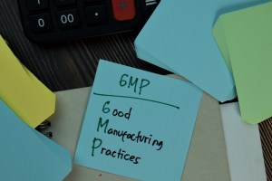 Sticky note with handwritten “GMP - Good Manufacturing Practices” placed among colorful papers and a calculator, representing GMP Certified Supplements. Highlights the importance of cGMP certification for dietary supplements and adherence to a GMP certified production process.