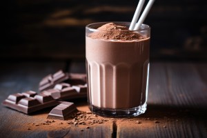 Chocolate protein shake with cocoa powder topping, alongside chocolate pieces. The powder used is indicative of products made by pre workout manufacturers USA and custom powder manufacturers, demonstrating the process of custom powder manufacturing