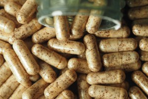 Close-up of natural herbal dietary supplement capsules with speckled contents, representing small batch supplement manufacturing, organic capsule formulation, and plant-based alternatives to synthetic substances.