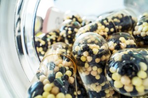 Close-up view of transparent capsules filled with small black, cream, and yellow spherical beads, stored in a clear container.