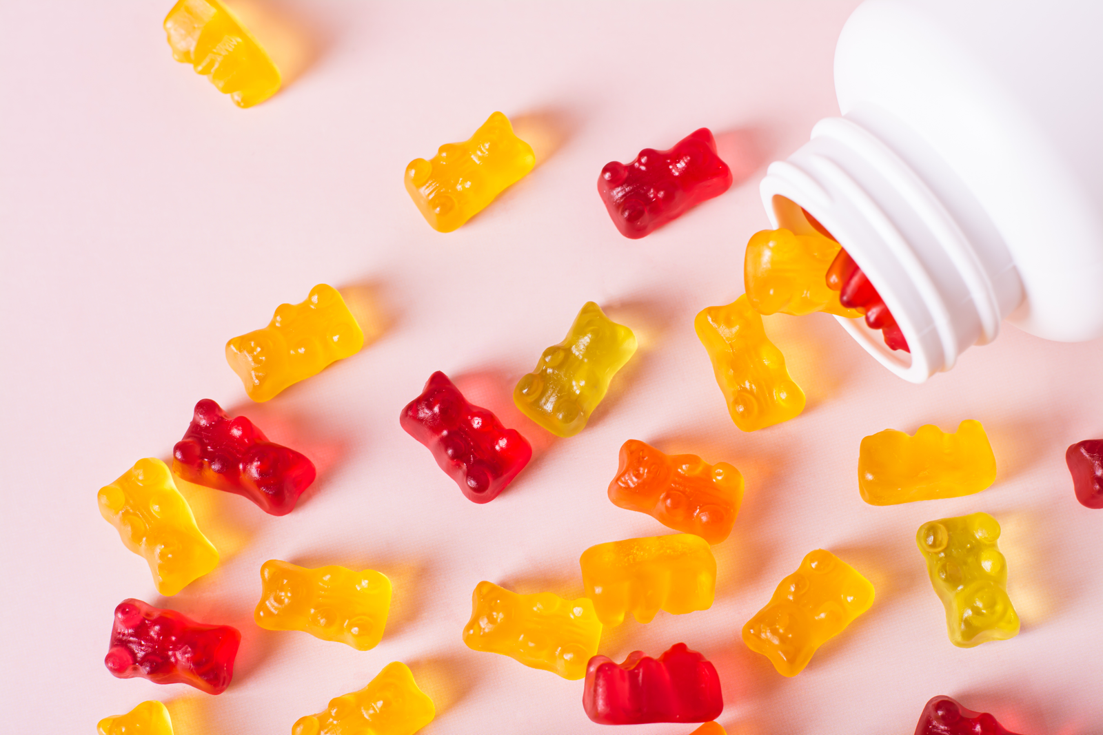 Yellow and red Gummy Supplements coming out of a white bottle on a pink background