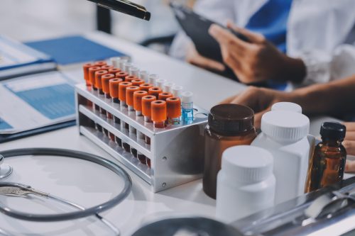 Medical laboratory with blood sample test tubes and supplement bottles on a desk, representing research, quality testing, and supplement formulation in healthcare.